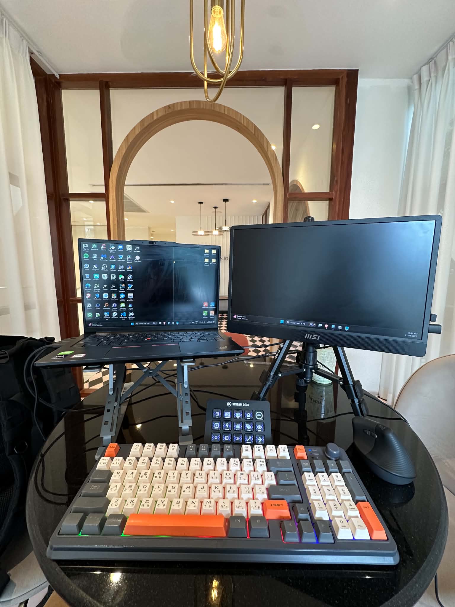 Portable desk setup: laptop on a stand, MSI portable monitor, Stream Deck, and a Thai-layout mechanical keyboard.